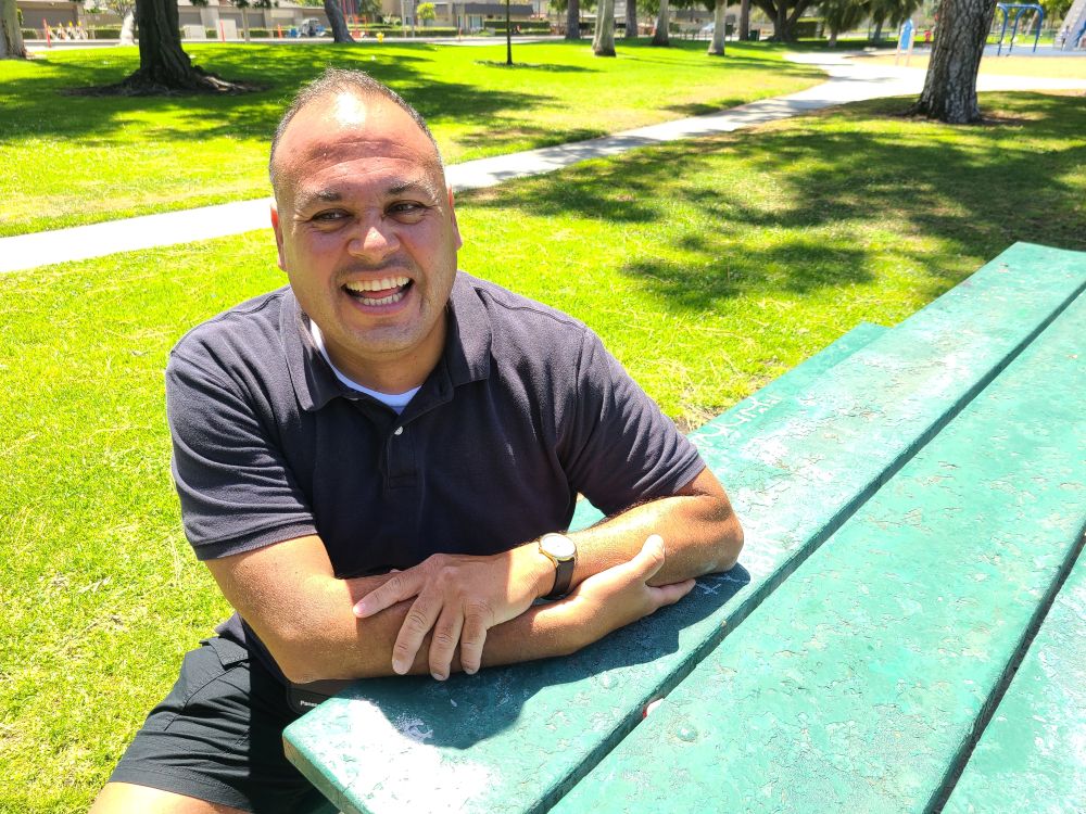Albert sitting on a park bench, in the sun, smiling
