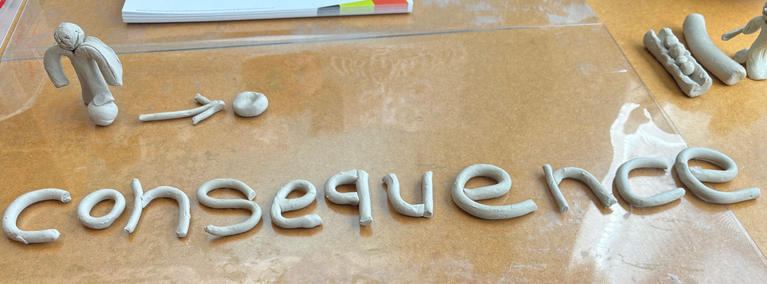 The word consequence spelled out in clay with a person stepping on a ball, an arrow pointing to a flattened ball.