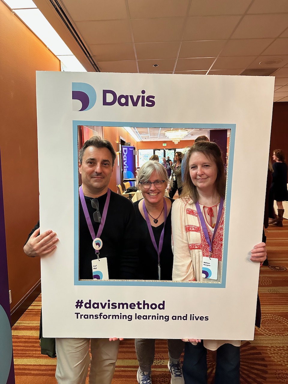 Three Davis Facilitators holding a Davis photo frame, they are standing inside the frame