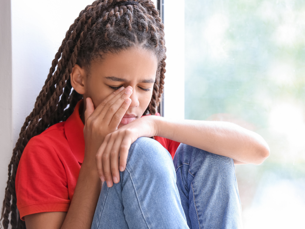 Young adult, looking upset with hand to her face, like she is crying