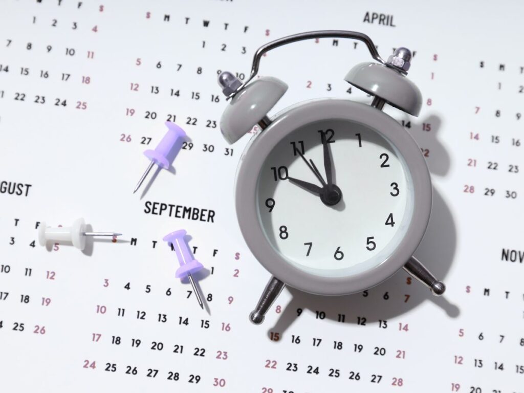 An image of an older, anologue alarm clock, sittong on a calendar