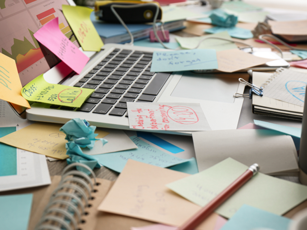 A desk with a laptop, the desk and laptop are covered in sticky notes and reminders. It is very chaotic