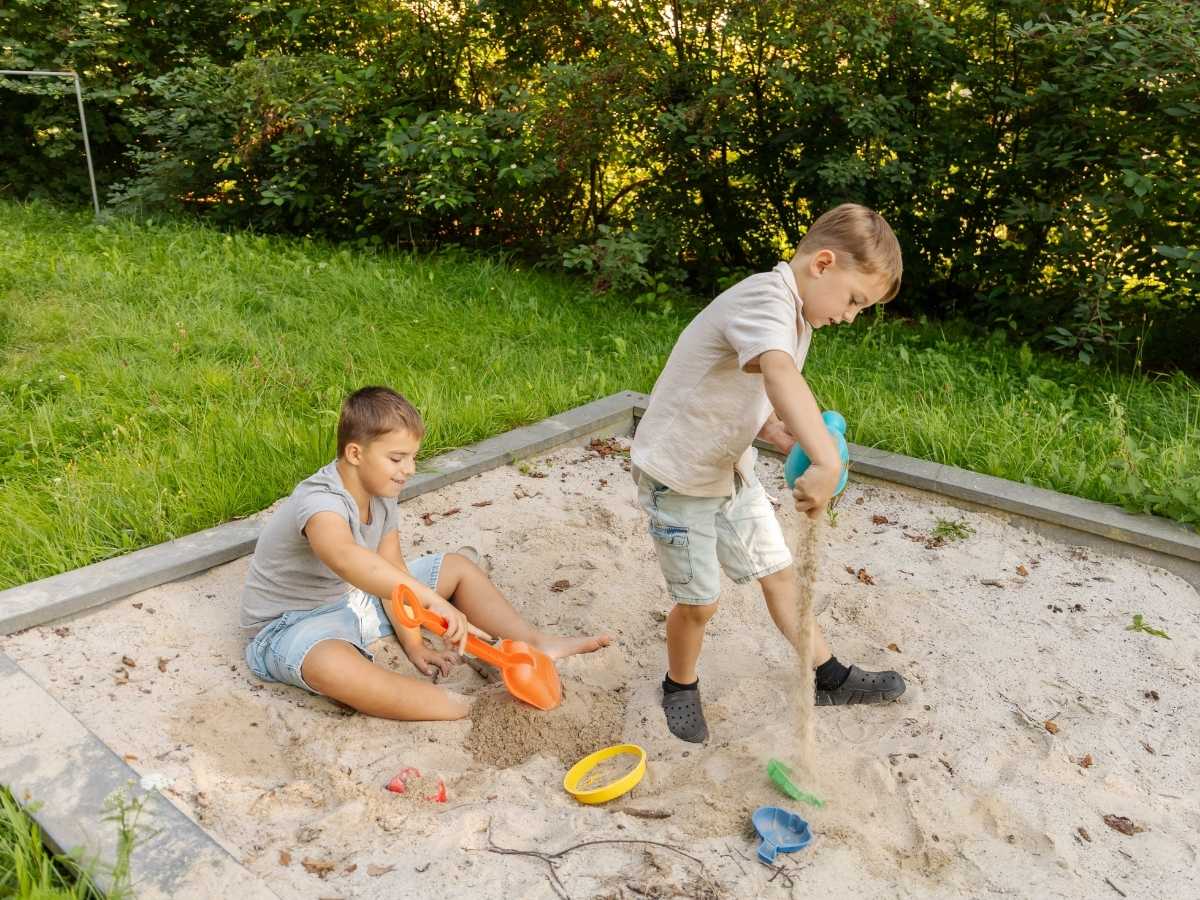2 young boys, around 8 years old, playing in a sandbox, surrounded by toys