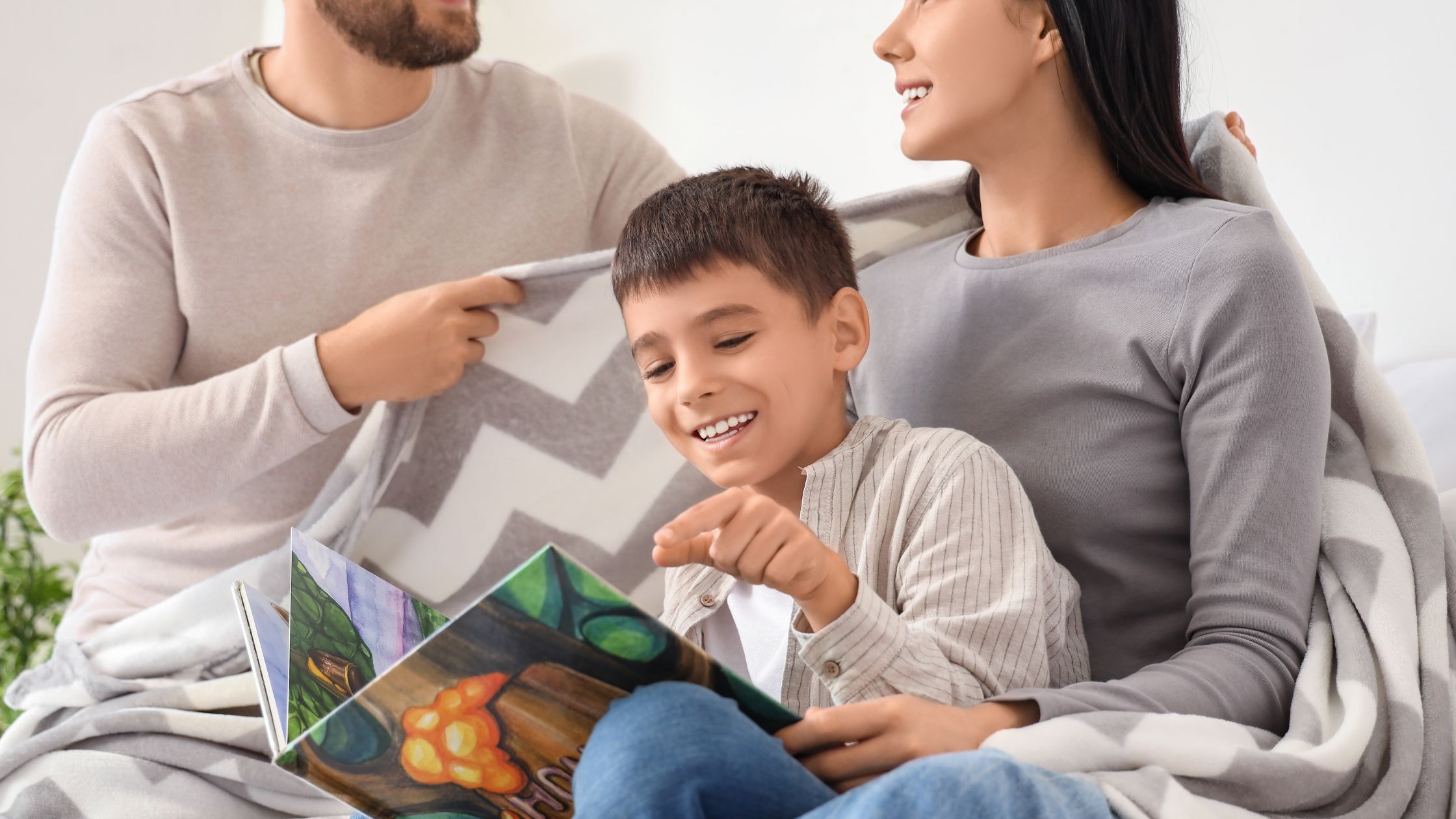 Family made up of a man, woman and child, sitting on a couch, the child is holding a book.